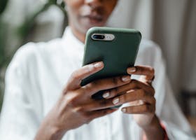 A woman in a white blouse using her smartphone indoors, showing a thoughtful and calm mood.